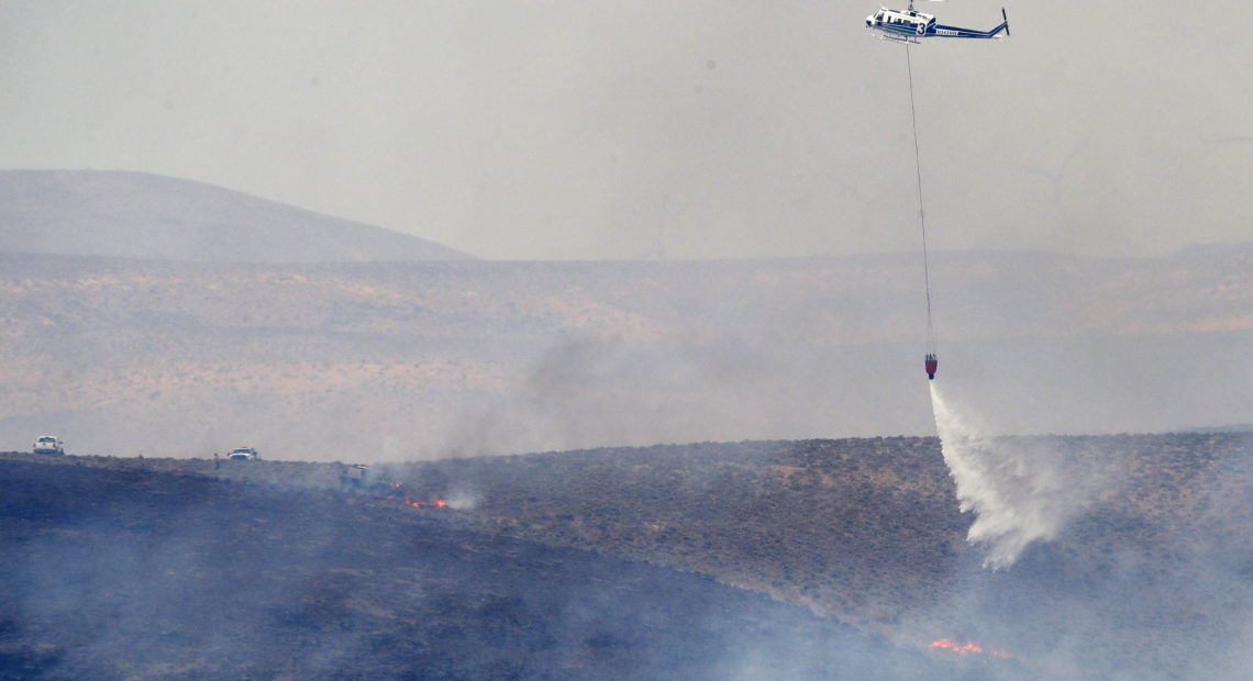 A helicopter uses a bucket to drop water on the Milepost 22 wildfire, Thursday, June 21, 2018, near Vantage, Wash. CREDIT: AP PHOTO/TED S. WARREN