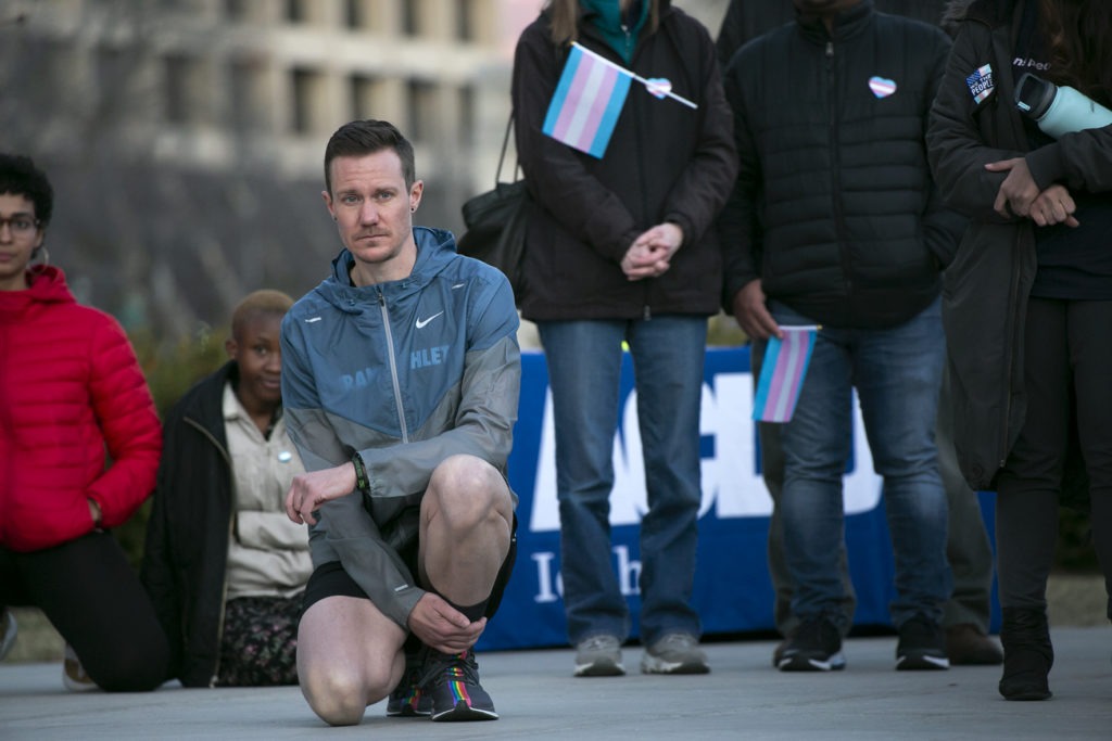 Chris Mosier, a Team USA athlete and transgender activist, kneels as he listens to speakers at a rally at the Statehouse on Tuesday, March 3 against Idaho’s HB500 banning transgender athletes from participating in women’s sports.