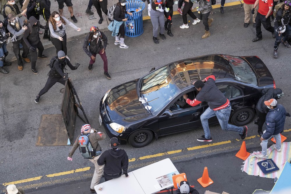 A man drives into the crowd at 11th and Pike, injuring at least one person, before exiting the car and brandishing an apparent firearm, Sunday, June 7, 2020, in Seattle, during protests over the death of George Floyd in Minneapolis. The man reaching into the car to stop it was injured. CREDIT: Rutz/The Seattle Times via AP