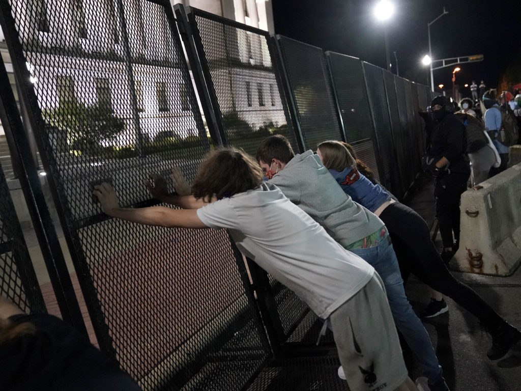 Protesters attempt to topple a fence outside the Kenosha County Courthouse late Tuesday in Kenosha, Wis. Protests continued following the police shooting of Jacob Blake on Sunday. CREDIT: David Goldman/AP