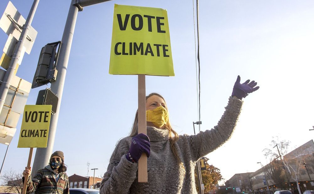 Kristin Green, left, and Kayla Bordelon, from the Citizens Climate Lobby, hold signs and wave to motorists on Election Day, Nov. 3, 2020, in Moscow, Idaho. CREDIT: Geoff Crimmins/The Moscow-Pullman Daily News via AP