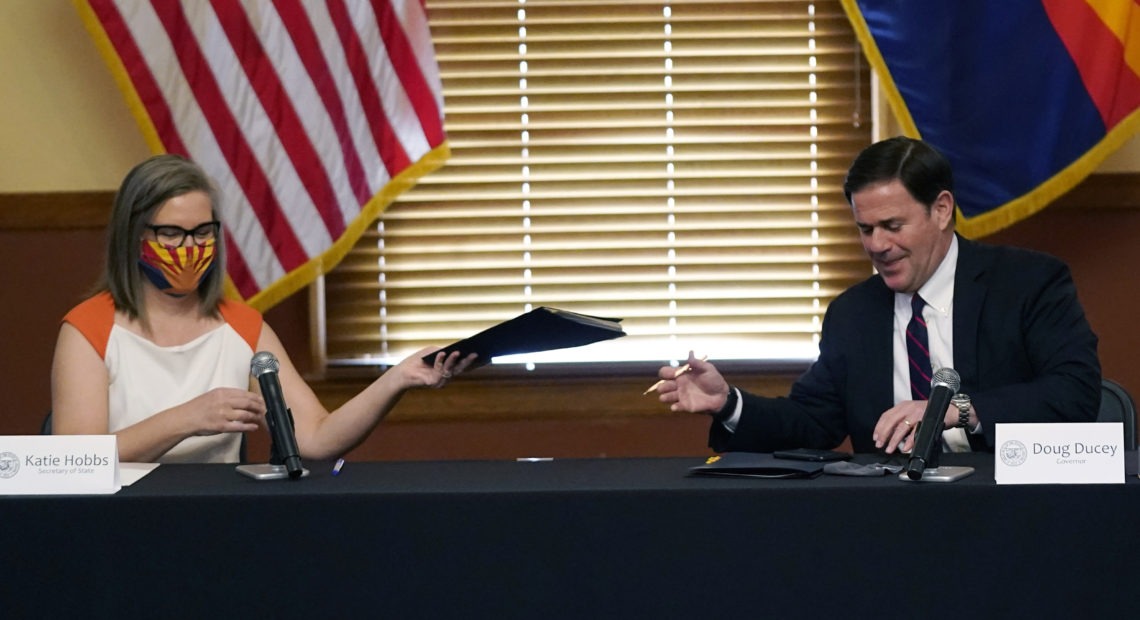 Arizona Secretary of State Katie Hobbs and Gov. Doug Ducey exchange election documents as they certify election results Monday at the Arizona Capitol in Phoenix. CREDIT: Ross D. Franklin/AP