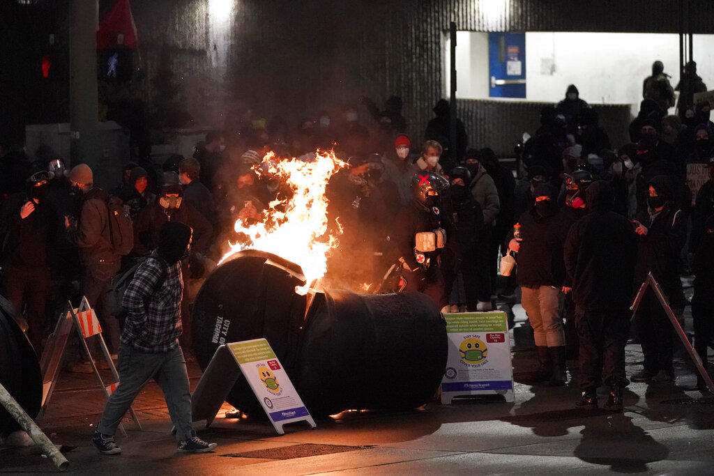 A trash can burns as people take part in a protest against police brutality, late Sunday, Jan. 24, 2021, in downtown Tacoma, Wash., south of Seattle. The protest came a day after at least two people were injured when a Tacoma Police officer responding to a report of a street race drove his car through a crowd of pedestrians that had gathered around him. Several people were knocked to the ground and at least one person was run over. CREDIT: Ted S. Warren/AP