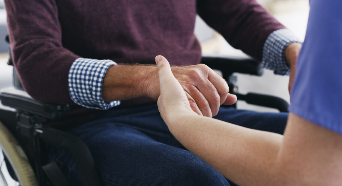 Cropped shot of a nurse holding hands with a senior man in a wheelchair