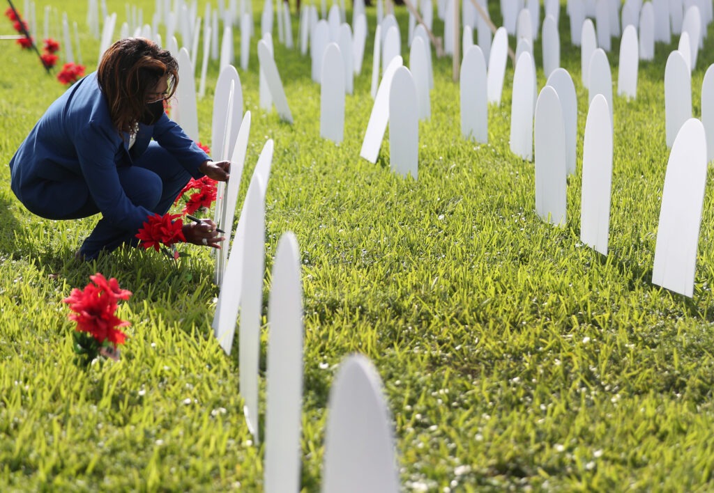 Mary Estime-Irvin, a councilwoman in North Miami, Fla., writes the name of a friend lost to COVID-19 on a symbolic tombstone that is part of a pandemic memorial at Griffing Park in North Miami in October. CREDIT: Joe Raedle/Getty Images