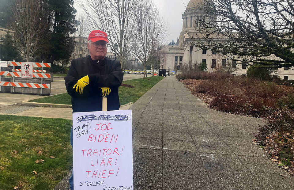 John Hess holding a sign describing President Joe Biden as a “traitor” and a “thief," as he stands outside a barricade set up by state troopers at the Washington state Capitol building, Jan. 20, 2021. CREDIT: Melissa Santos/Crosscut