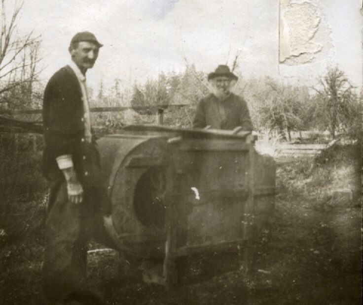 Black pioneer George Bush's grandson, left, and son, right, stand next to a fanning mill on the family's farm near present day Tumwater, Washington. A monument to George Bush and his family is planned for Washington's Capitol Campus. CREDIT: Washington State Historical Society