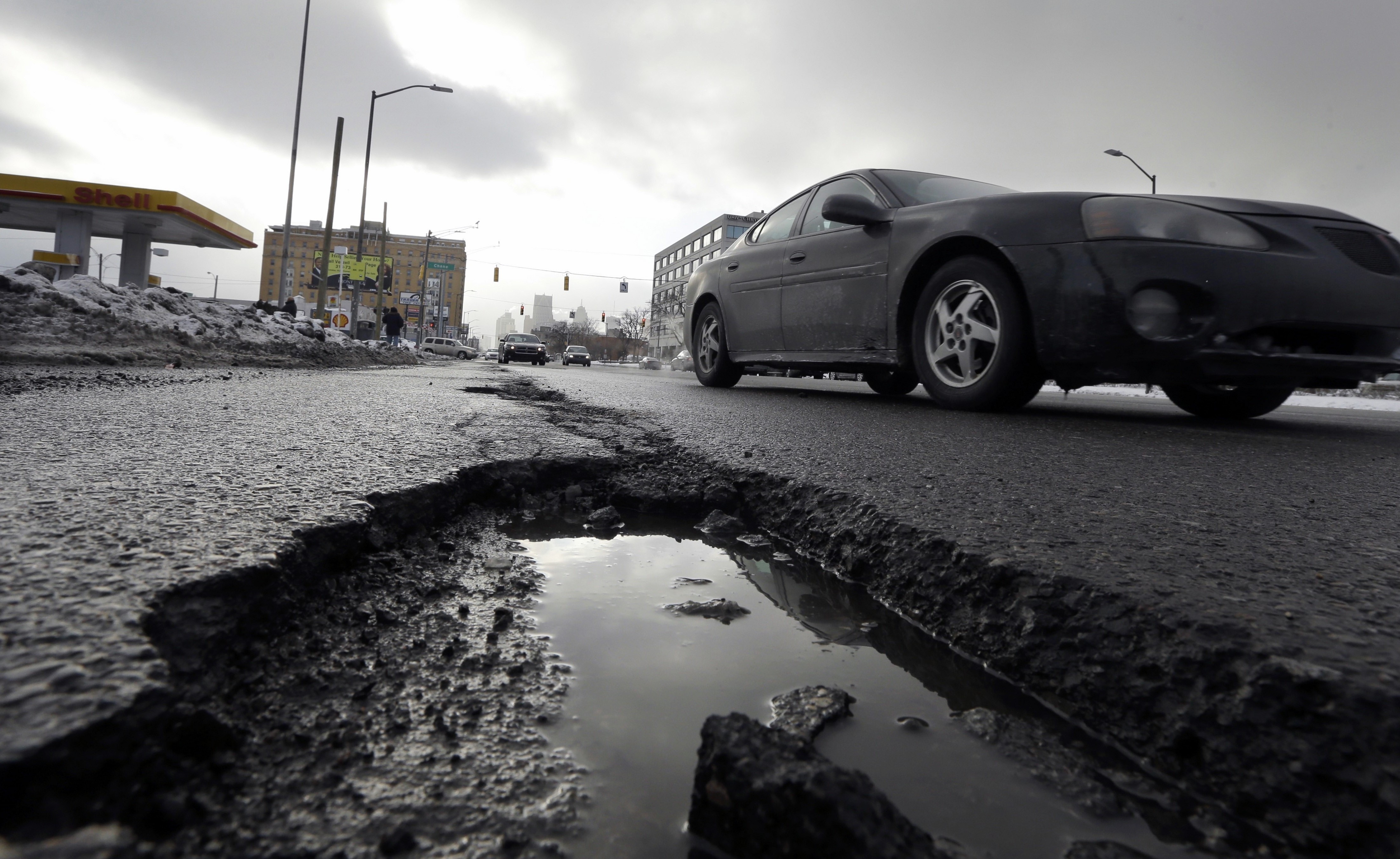 In this Feb. 11, 2014 photo a car drives by a pothole in Detroit. The relentless cycle of snow and bitter cold this winter is testing the skeletons of steel and cement on which communities are built. Pipes are bursting in towns that are not used to such things, and roads are turning into moonscapes of gaping potholes big enough to snap axles of passing vehicles. (AP Photo/Carlos Osorio)