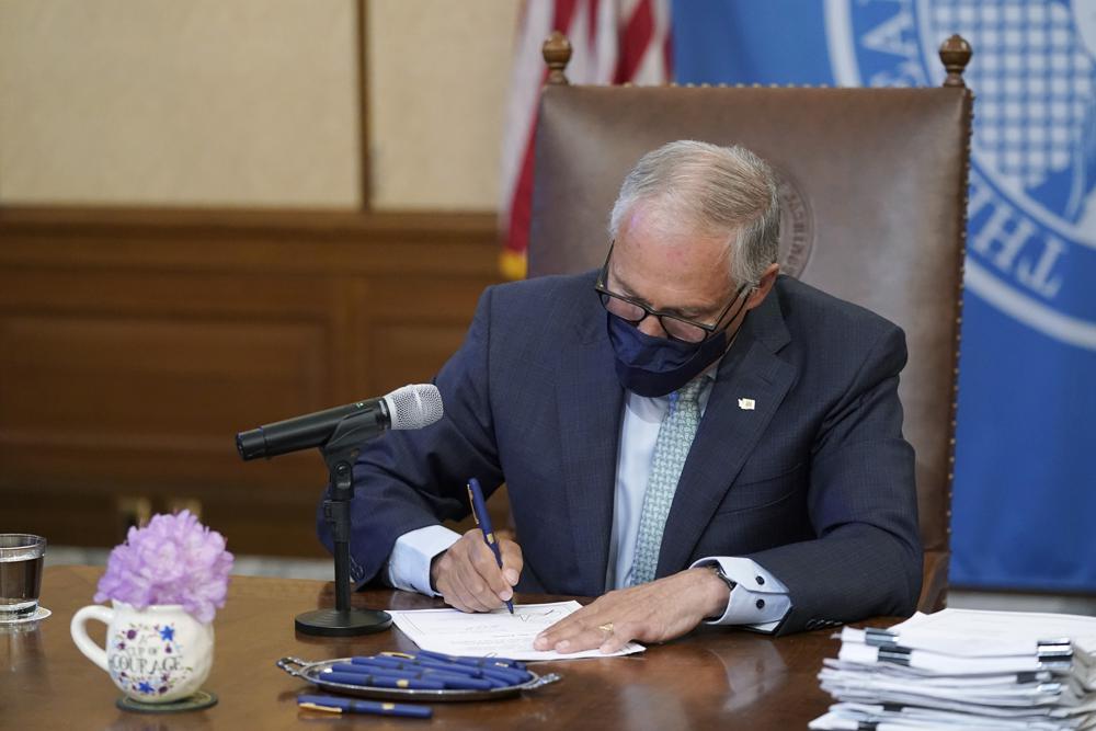 Washington Gov. Jay Inslee signs a bill into law on May 12, 2021, at the Capitol in Olympia, Wash., that prohibits openly carrying guns and other weapons at the state Capitol and protests statewide. CREDIT: Ted S. Warren/AP