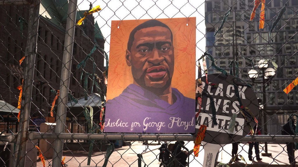 A picture of George Floyd hangs on a fence barrier that surrounds the Hennepin County Government Center in Minneapolis during the trial of former police officer Derek Chauvin in March. The Justice Department is now bringing criminal charges against Chauvin over allegedly violating Floyd's rights and using excessive force in restraining him. CREDIT: Scott Olson/Getty Images