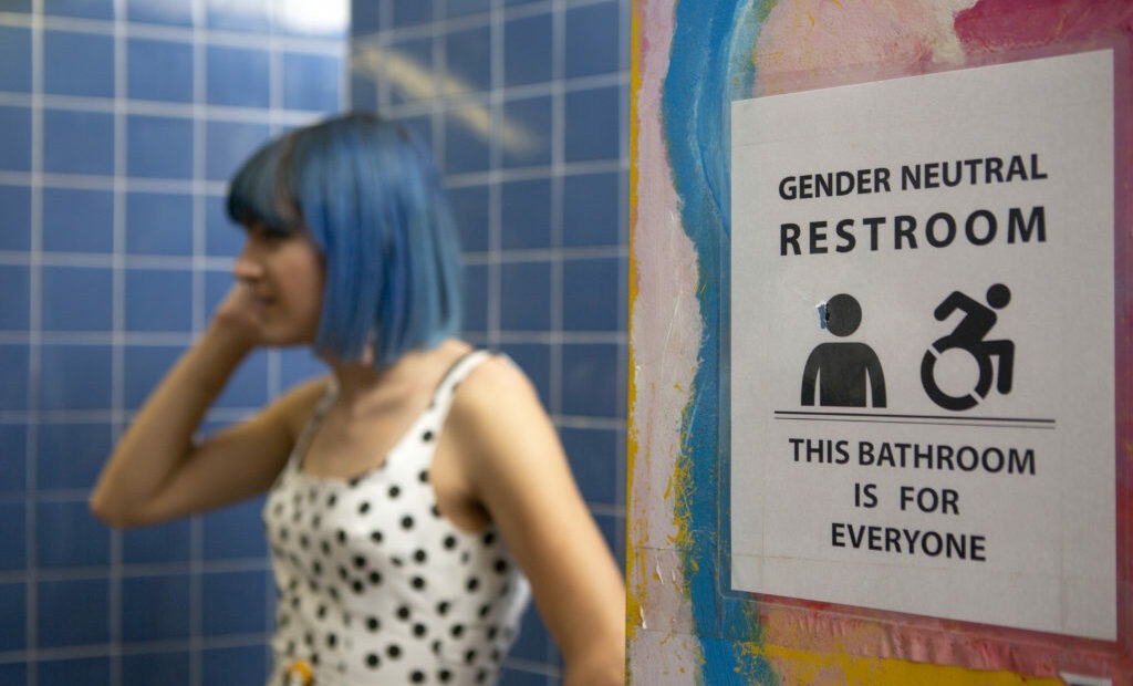 A nonbinary person next to gender-neutral sign to a bathroom. Photo by Zackary Drucker/Broadly’s Gender Spectrum Collection