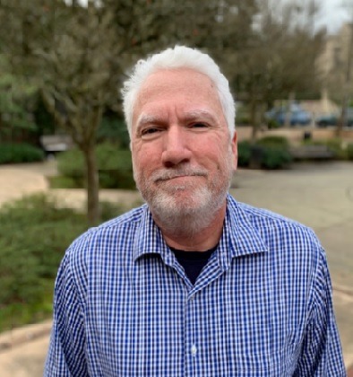 Photograph of Tom Carpenter wearing a blue shirt with white hair and white goatee