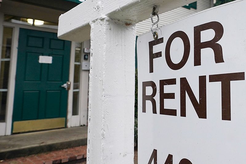 A white for rent sign hands in front of a home with a dark blue door.