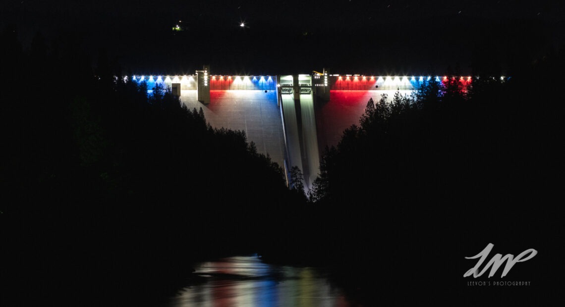 The Dworshak Dam glows red white and blue surrounded by the black of night.