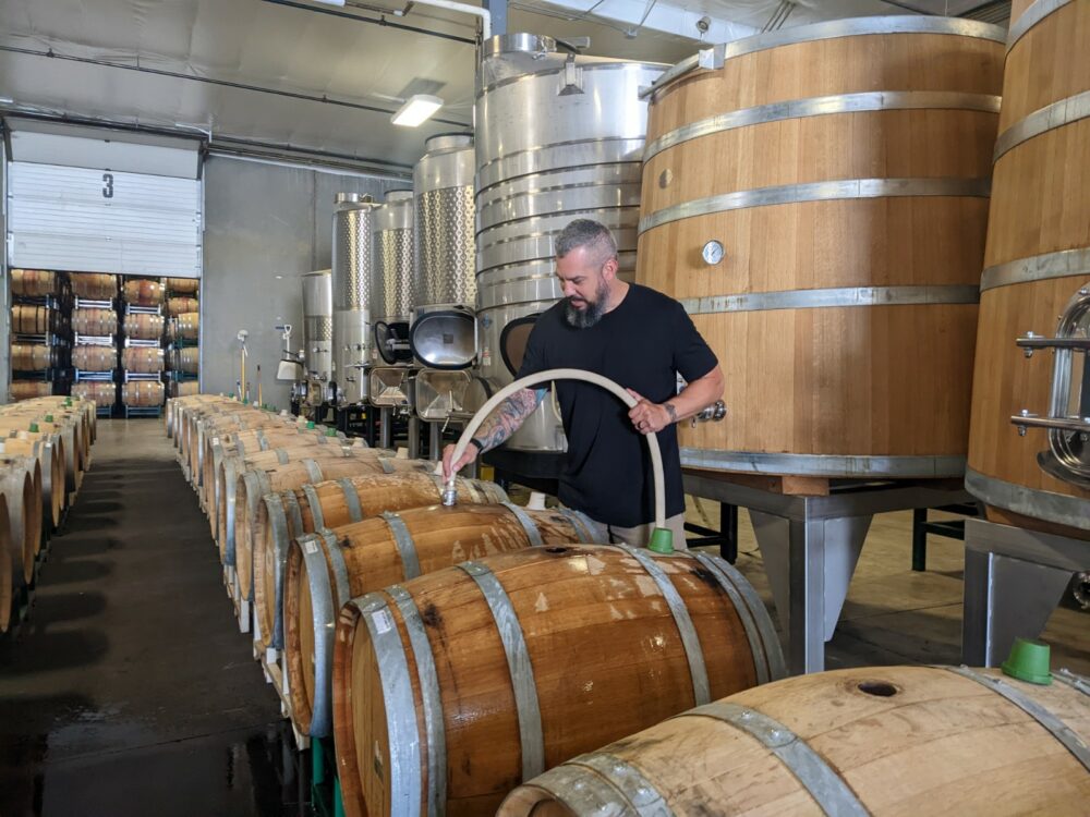 A tall man with a beard sprays down wooden wine barrels.