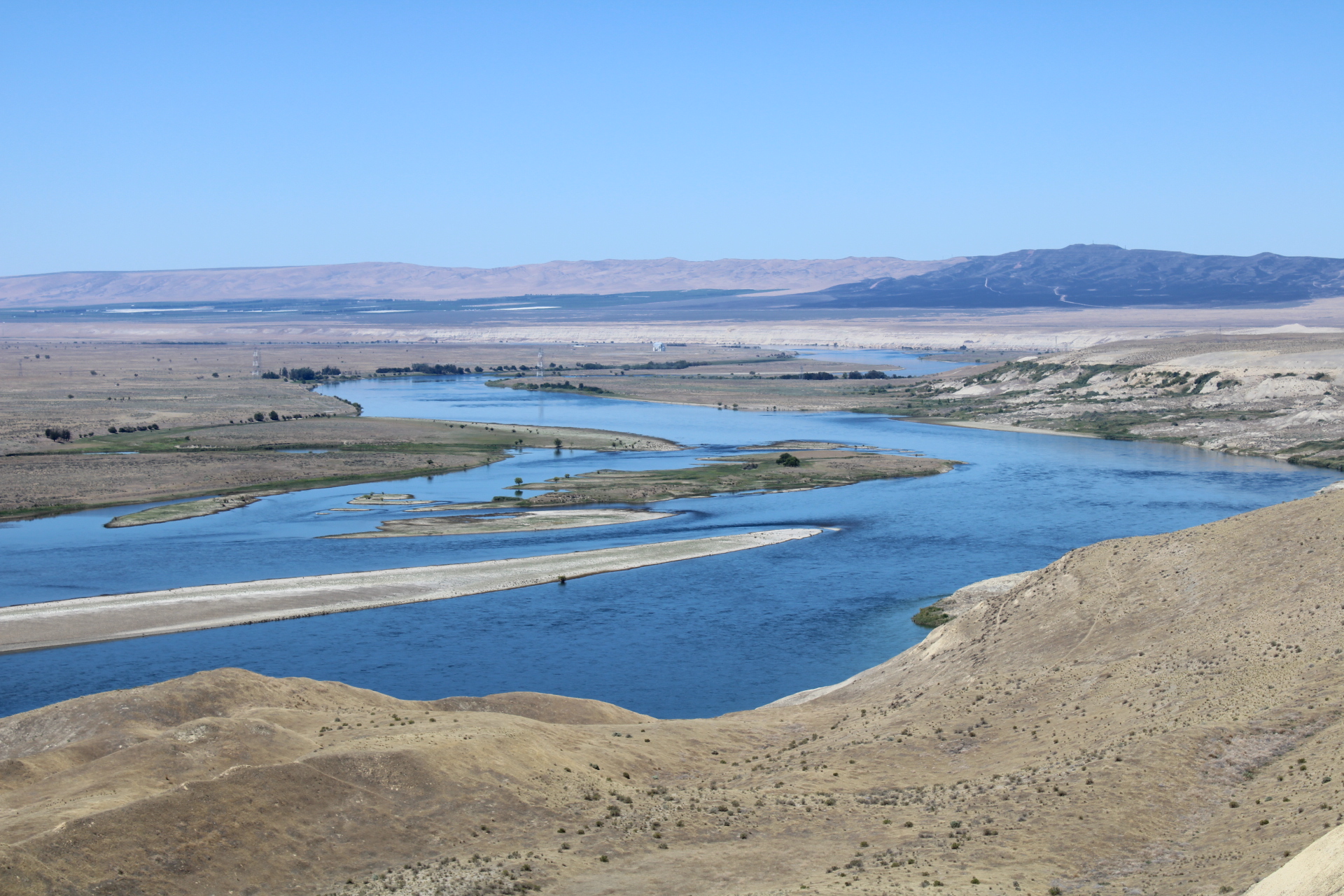 A scenic overview of the blue Columbia River from a bird's eye view shows nuclear reactors in the distance.