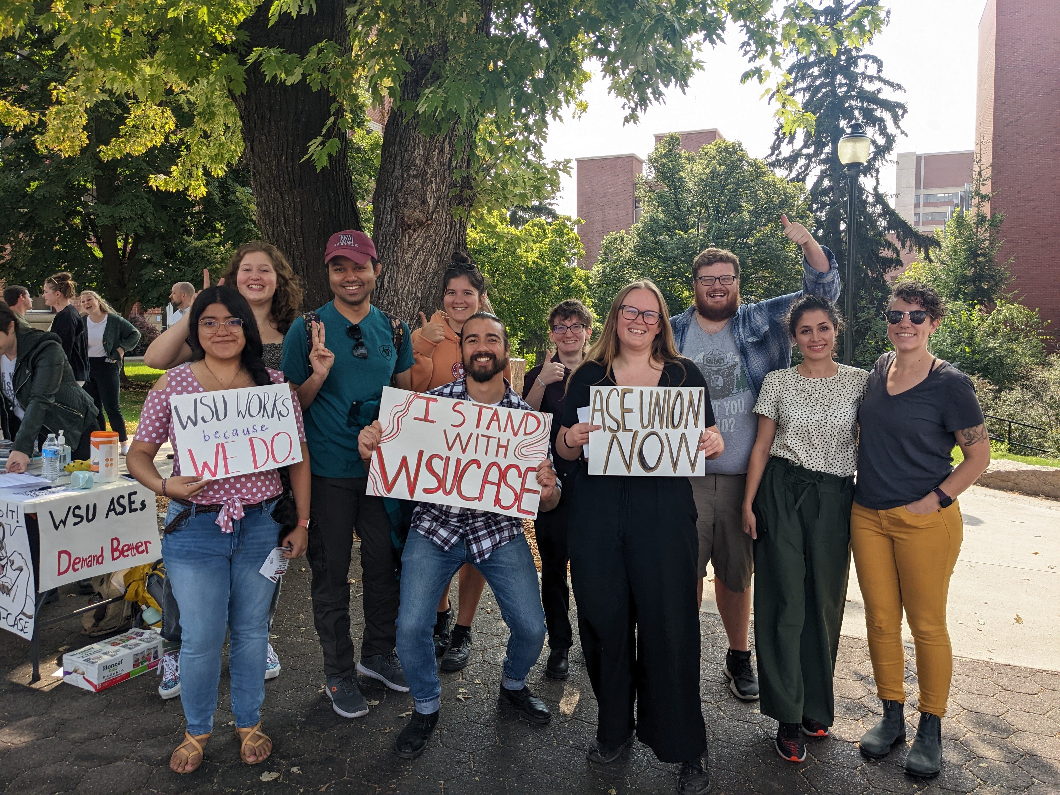 WSU Students stand beneath a tree in front of the CUB with hand written signs in support of a student workers union.