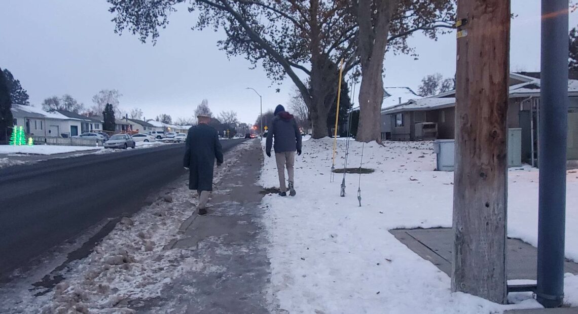 two people walking on an icy sidewalk one in the street