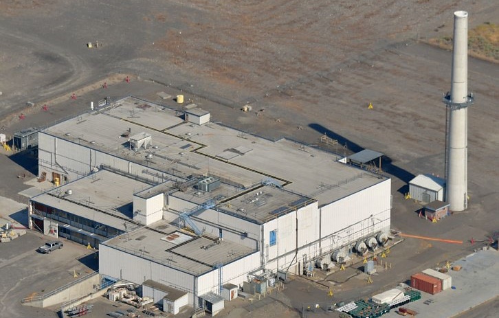 A large rectangular white, ware-house looking building is pictured on a paved strip of land.