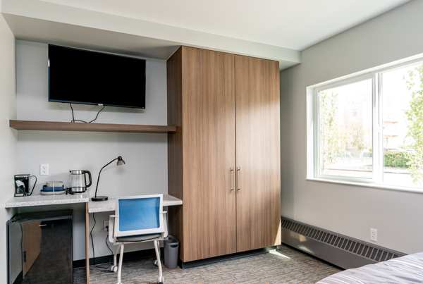 An image shows a small desk, TV and dresser in a room with a window. 