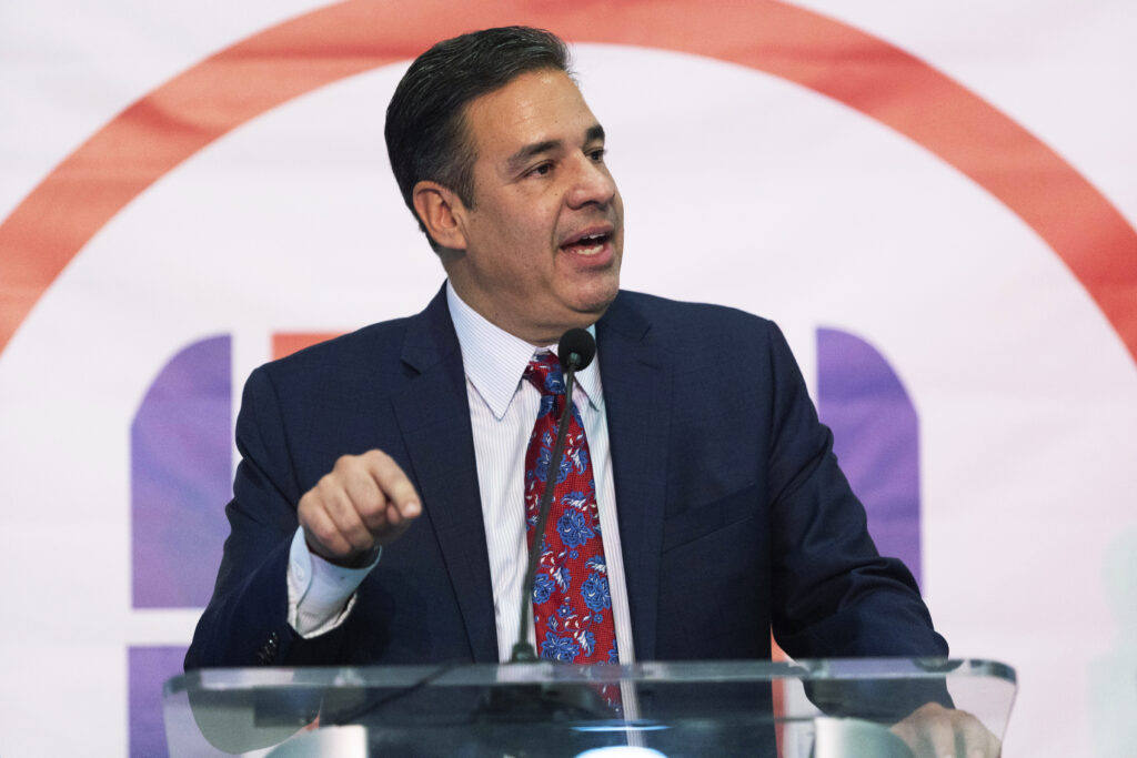 Raul Labrador stands at a podium in a navy blue suit. 