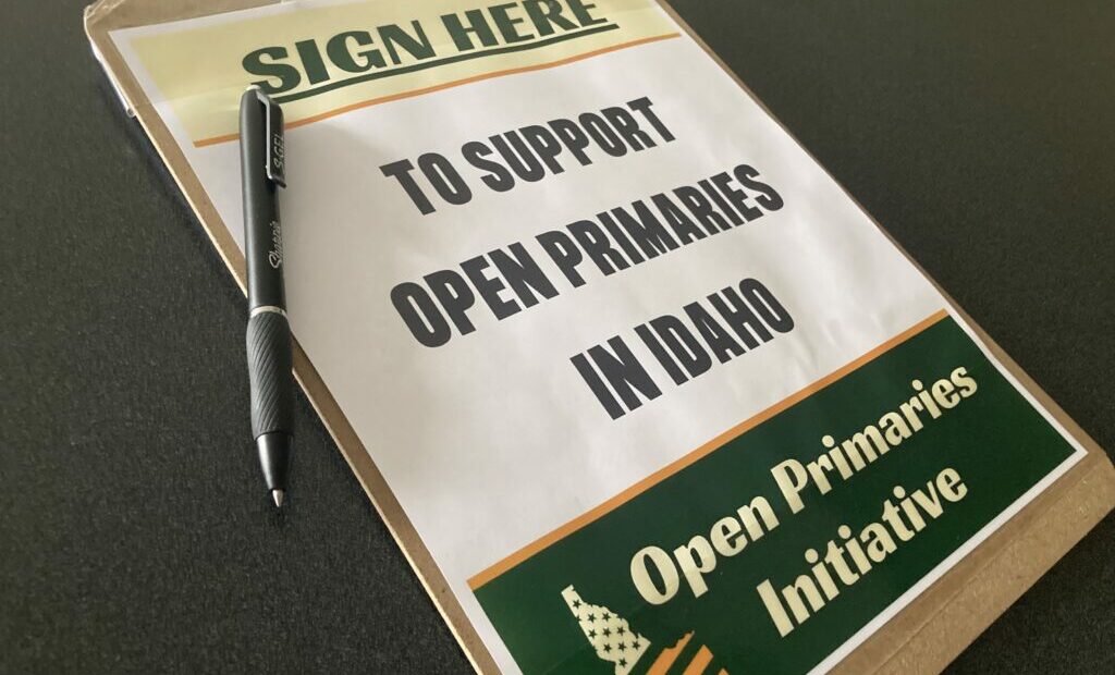 A clipboard reads "sign here to support open primaries in Idaho" in green lettering.