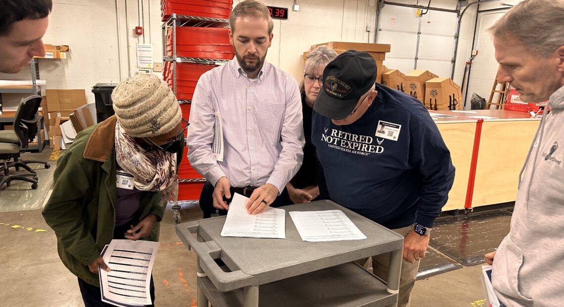 Kyle Haugh stands with election observers as they go through the zeroes report, showing that no ballots are sitting in the system. (Credit: Lauren Gallup / NWPB)