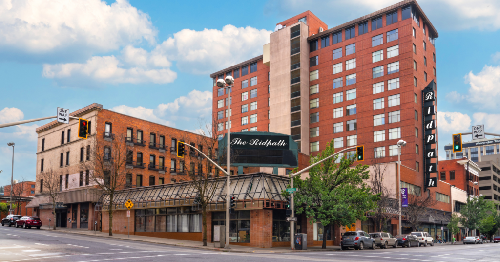 A large brick building against a blue sky has a black sign reading "The Ridpath" in front of it. 