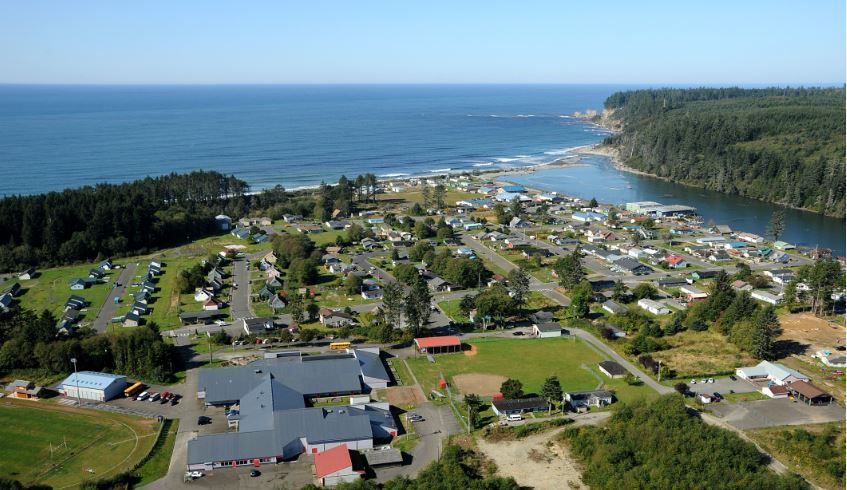 An aerial photo shows the lower village of Taholah near a bright blue ocean.