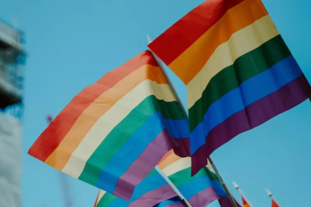 Pride flags fly in the wind against a clear blue sky