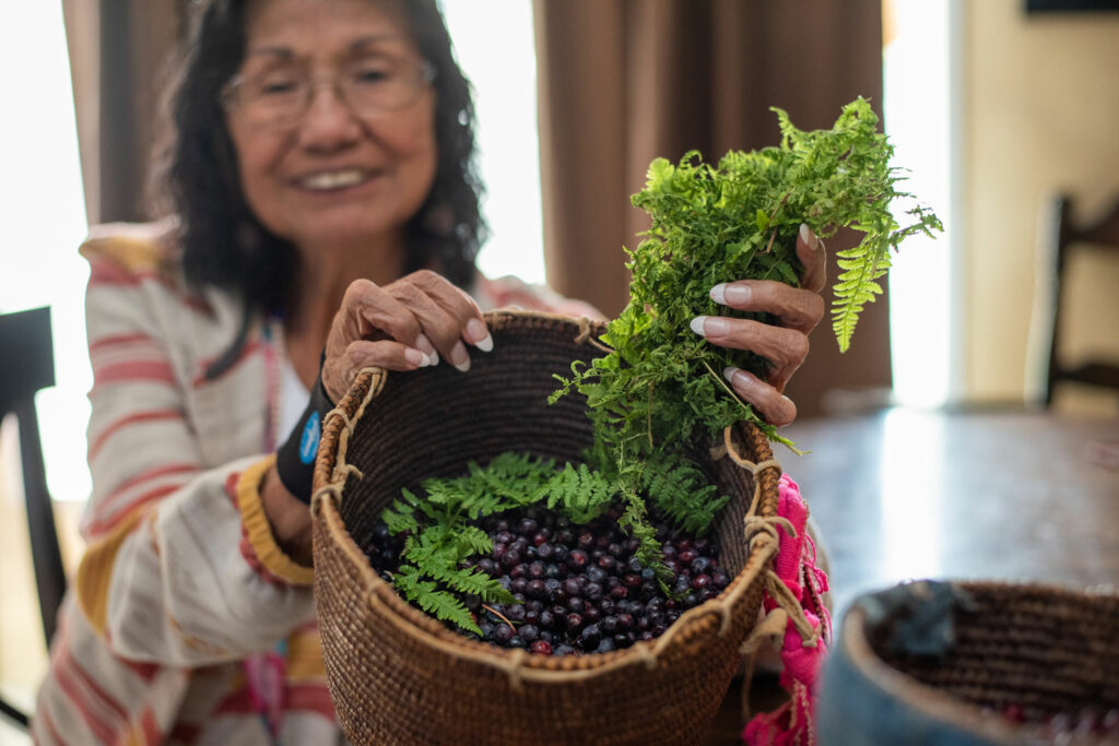 A woman holds a woven basket filled with dark purple huckleberries.