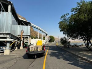 A gray truck with a white tank and tan coolers in its bed drives away down a road with a yellow stripe down the center.