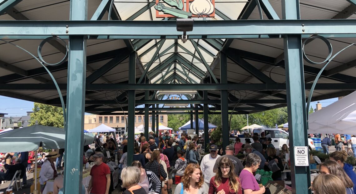 A group of people walk through vendor stalls at the Walla Walla Downtown Farmers market.