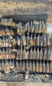 Shelves of burned wine bottles sit stacked on top of each other covered in dirt dust. 