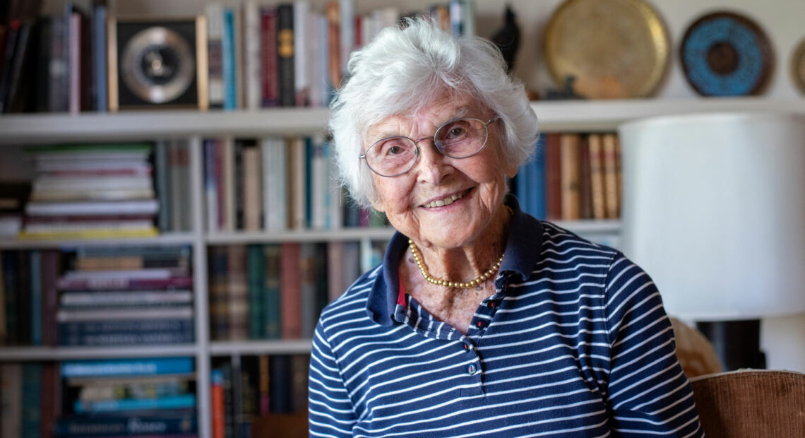 A portrait of Virginia Hislop in her living room with books behind her.