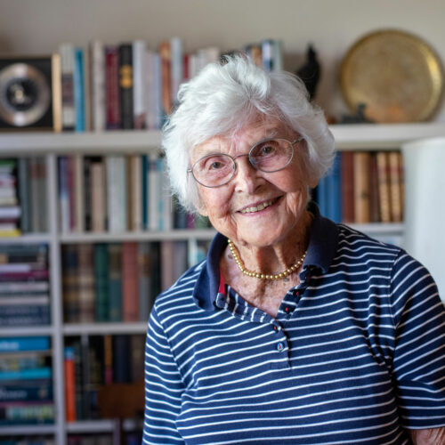 A portrait of Virginia Hislop in her living room with books behind her.