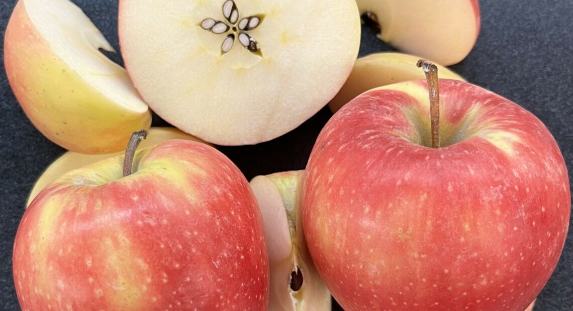 The photo shows whole apples covered in light orange, yellow and blush skin. Some apples are sliced open to reveal a white interior.