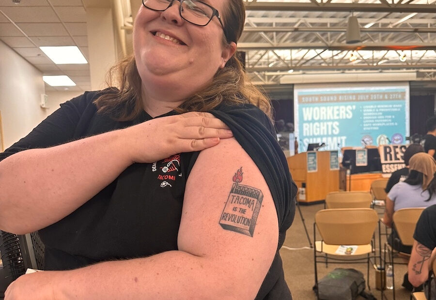 Ann Dorn, who serves on the steering committee of Tacoma for All, poses at the workers' rights event with the tattoo she got after the group's initiative for a tenant bill of rights passed in 2023. (Credit: Lauren Gallup / NWPB)