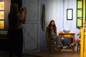 Christy Reich takes photos of grandchildren Cassia Enson and Callen Woods in a recreation of Vincent Van Gogh’s painting “The Bedroom” at "Van Gogh: The Immersive Experience" on July 29 in Spokane. (Credit: Rachel Sun / NWPB)