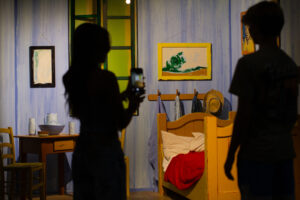 Cassia Enson and Callen Woods take photos of a recreation of Vincent Van Gogh’s painting “The Bedroom” at the exhibit. (Credit: Rachel Sun / NWPB)