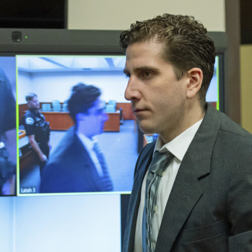 Man in suit in front of a TV screen.