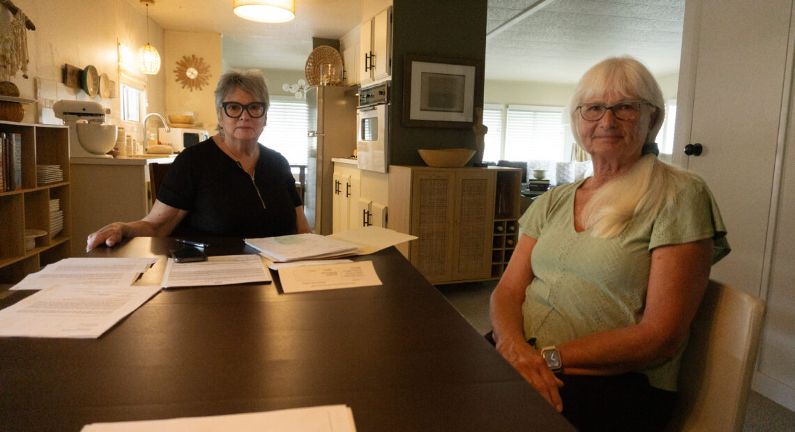 Two women look at the camera with papers before them.