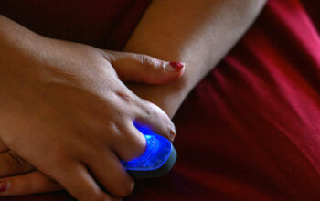 A large blue ring is on a person's finger. The ring is lit up, and is glowing.