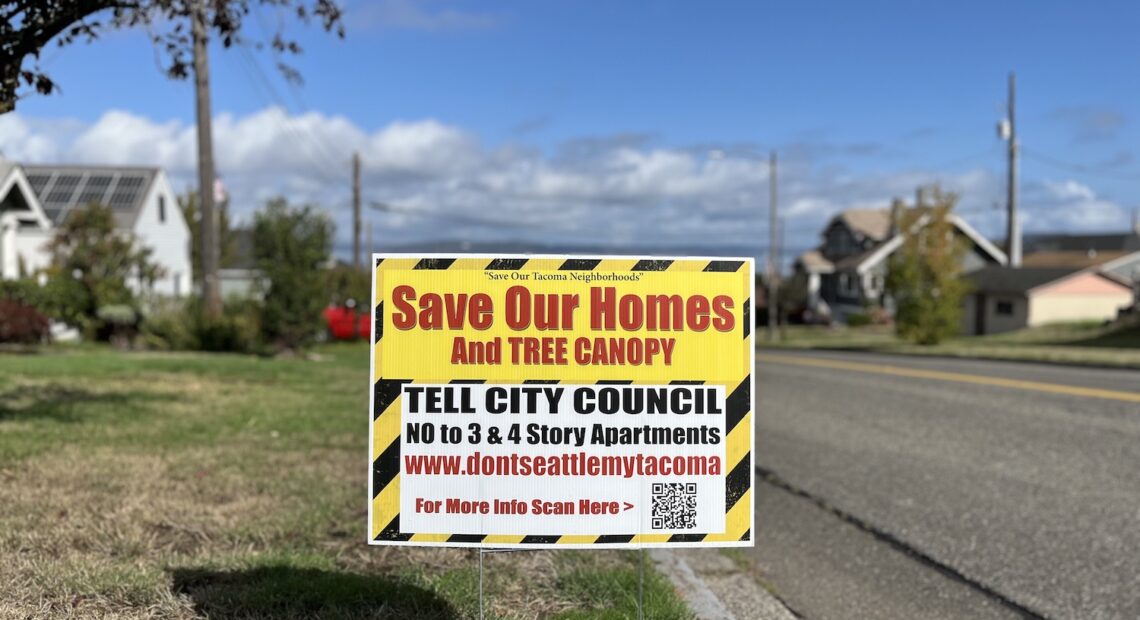 A bright yellow and black sign is placed in a front yard. Some of the text, in red letters, reads: "Save our homes and tree canopy."