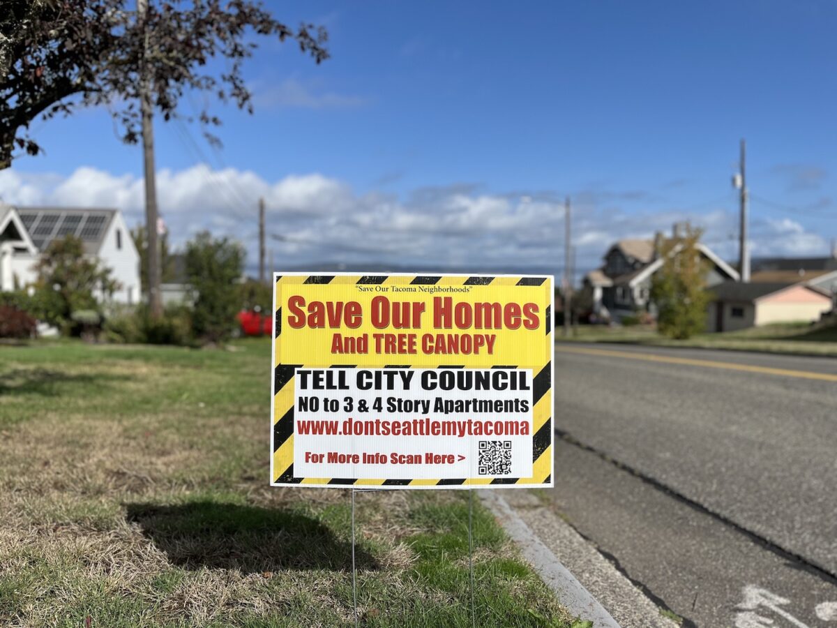 A bright yellow and black sign is placed in a front yard. Some of the text, in red letters, reads: "Save our homes and tree canopy."