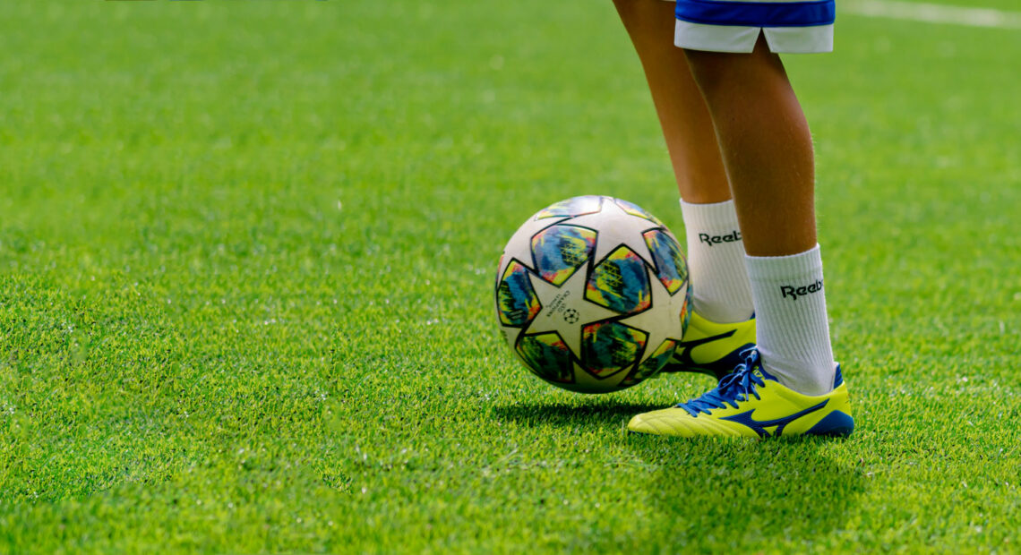 A teenager kicks a soccer ball on a pitch.