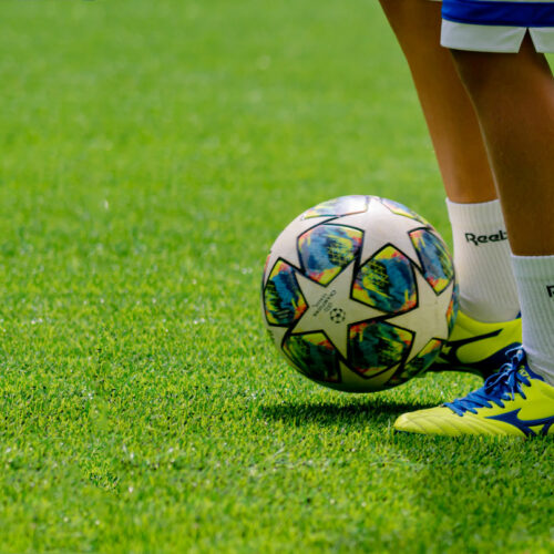 A teenager kicks a soccer ball on a pitch.