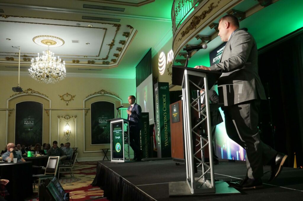 Two men, each behind a podium, stand on a stage.