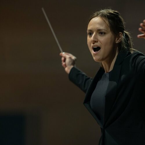 A woman holds a conductor's baton. She is conducting an orchestra.