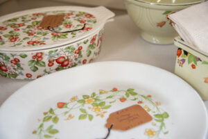 Vintage dishes sit on top of a white table. The dishes have red, orange and yellow flowers and green leaves on them.